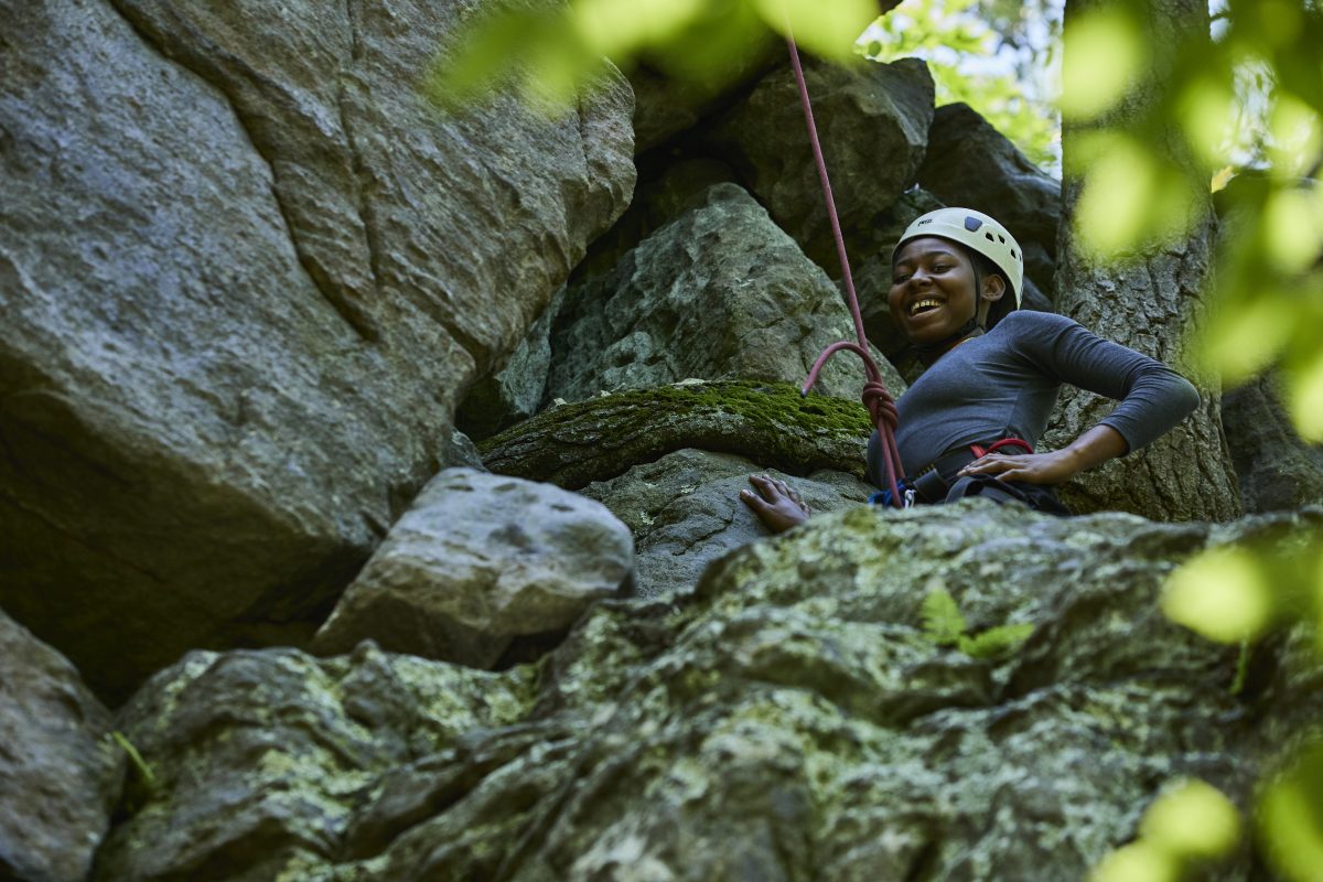 A female ROTC cadet climbs a rock face and is looking down smiling. Photo by Justin Durner.