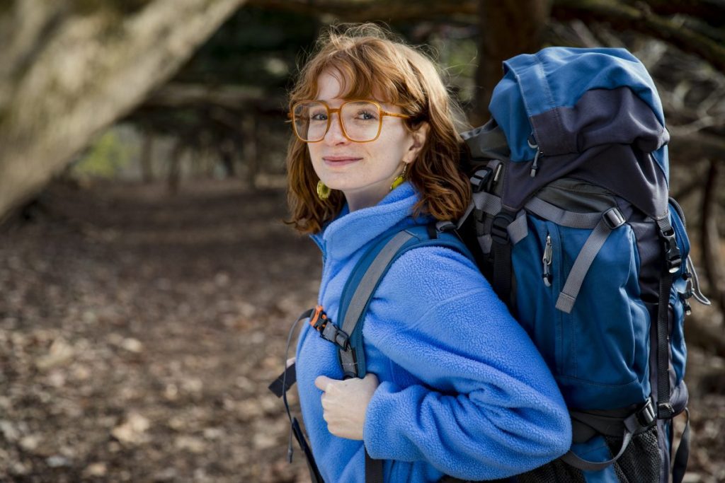 A portrait of Outward Bound instructor Chloe looking proudly into the camera and smiling. She wears a fleece jacket and a backpacking pack.