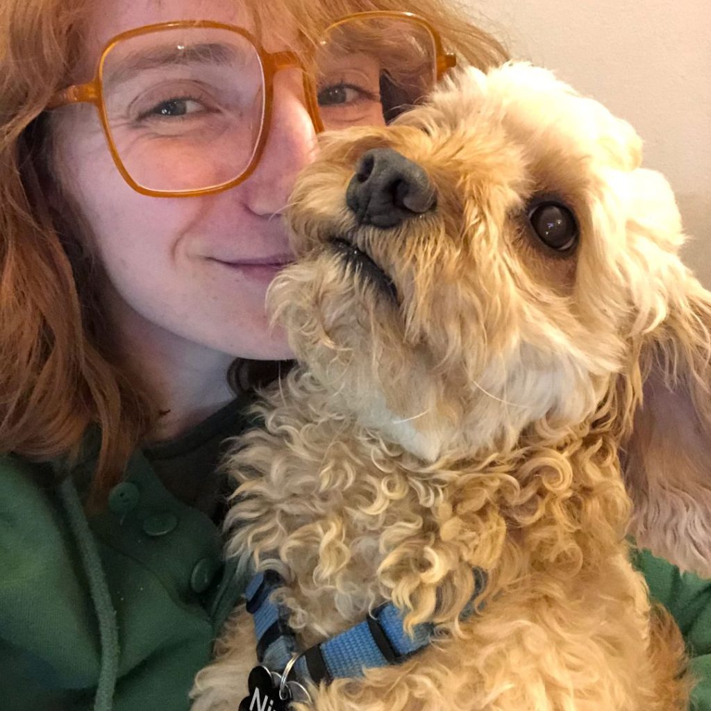 A selfie of Outward Bound instructor Chloe smiling with her dog Ninja. Ninja is a medium sized tan wavy haired dog with big brown eyes and long ears. 